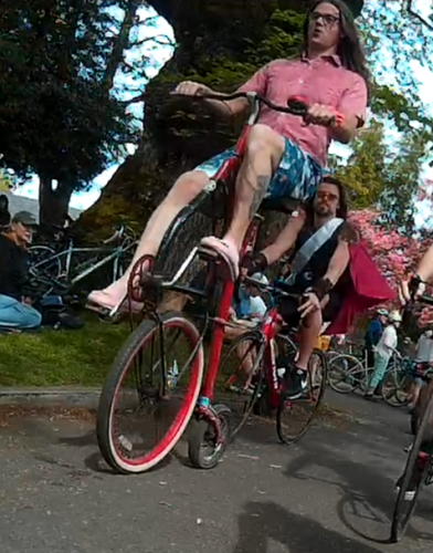 a person riding a tall bike with the rear wheel as the front of the bike and a seat + steerer on top of a penny-farthing style rear wheel