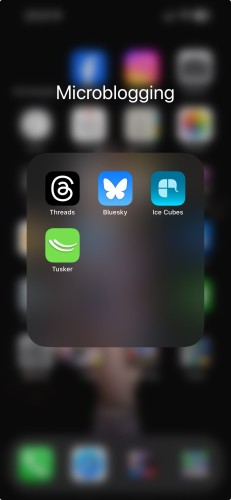 Screenshot of a folder on my iPhone Home Screen. The folder is labelled “Microblogging” and contains four Apps: Threads, Bluesky, Ice Cubes and Tusker. Ice Cubes and Tusker are Mastodon clients.