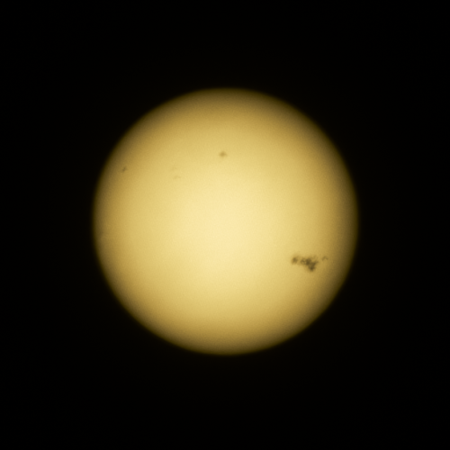 A picture of the Sun taken with a DSLR camera through crossed polarisers to make it faint enough. There are several dark sunspots seen on the Sun, including a very large group to the righthand side.