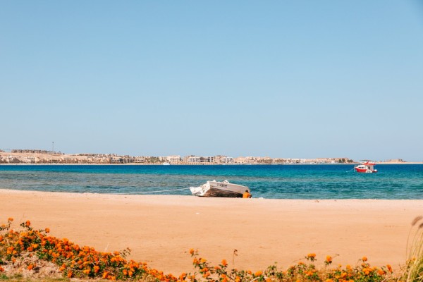 photo of a man sitting by his boat at the beach at a beautiful sunny day with a clear sky