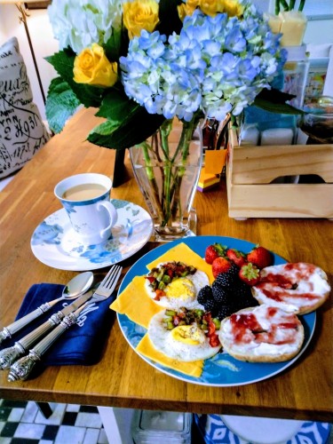 Two fried eggs with sliced cheddar cheese alongside strawberries and blueberries and two bagels topped with cream cheese and strawberry jam
With a side cup of coffee