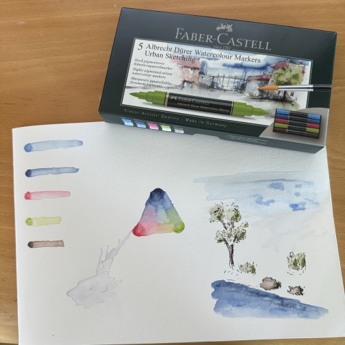 Box of 5 Faber-Castell Water Color markers and a paper with color swatches, blended colors and a small doodle of a tree and some rocks