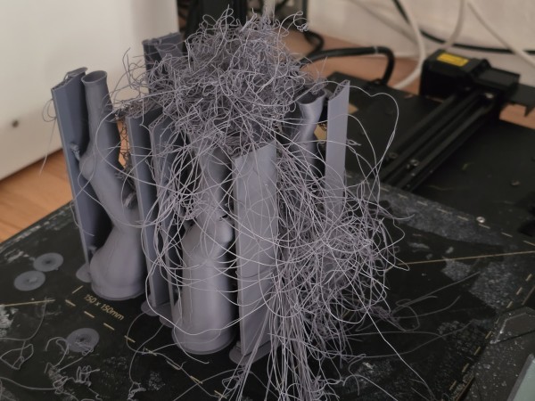 Auf dem Druckbett eines FDM-Printers, type "bedslinger" steht ein gefailter Print aus grauem PLA. vertikale struturen, mit Tree-Support. Ein wildes Gestrudel von Filament-Spaghetti oben drauf. 