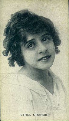 Black and white photo. Her hair is dark and curly. She is wearing a white dress or blouse (It is not visible on the photo what it is exactly). The name "Ethel Grandin" is written on the bottom in capital letters.