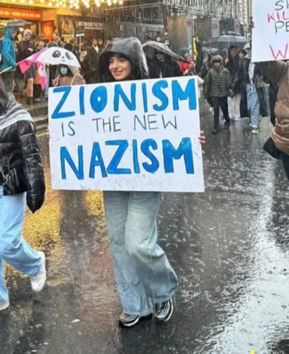 Image of a young woman walking in the rain, carrying a sign reading:
"Zionism is the new Nazism"