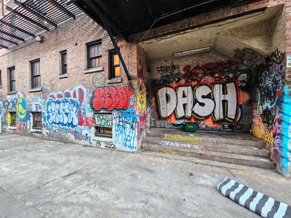 Colorful graffiti with bubble letters and bubble words across the rear of an old downtown brick building from the dirty alleyway behind.  One identifiable word is "Dash," possibly the graffiti artist's name?