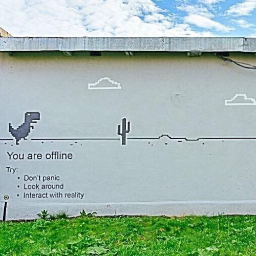 Wall art of a dinosaur in a pixel game scene of desert and tiny clouds, with the slogan You are Offline, Dont panic, Look around, Interact with reality

