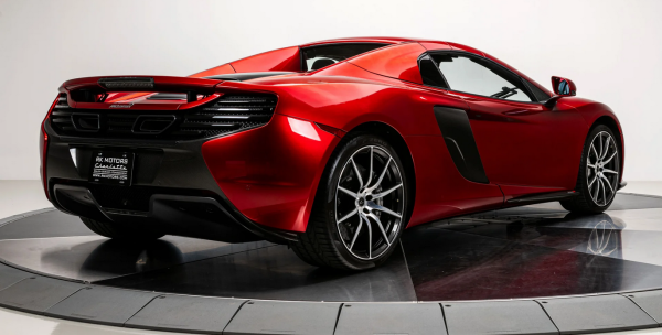 a jewel-red sports car, seen from behind in a three quarter view, really smooth and graceful and aerodynamic looking 
