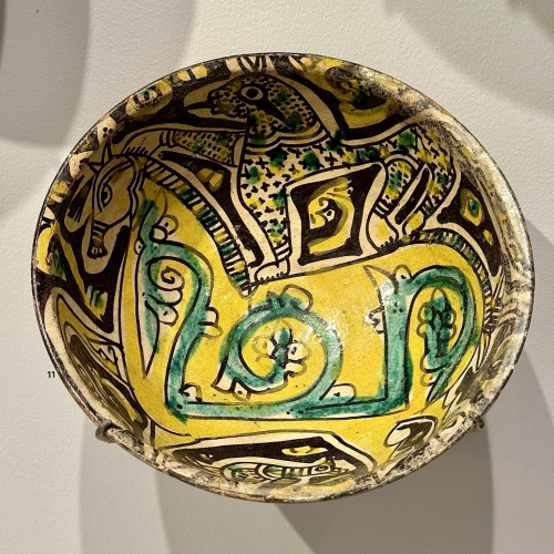 Bowl with a Cheetah Standing on the Back of a Horse Buff-colored earthenware painted with black (manganese and iron), yellow (lead-tin), and green (copper) under clear lead glaze Underglazed, painted 7.4 x 18.6 cm (2 15/16 x 7 5/16 in.) The range of the objects in this case illustrates the Islamic empire’s rapid expansion and the assimilation of peoples and artistic practices. A hot-worked glass vessel and a green-glazed pottery cup demonstrate continuity with late Roman traditions, while the figural imagery and inscriptions on tenth-century polychrome pottery vessels from eastern Iran underscore the continued vitality of pre-Islamic cultural traditions there.  https://harvardartmuseums.org/collections/object/165419