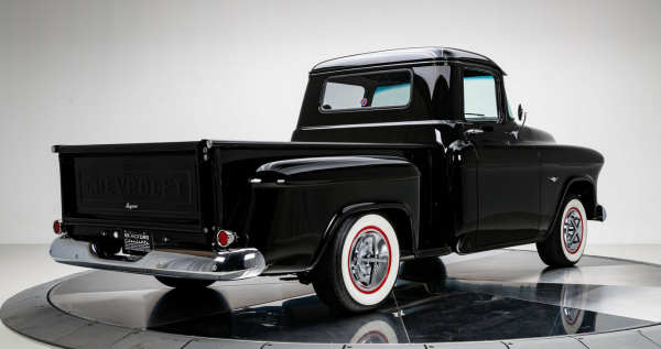 a photo of a black 1957 chevy pickup truck, seen from behind in a three quarter view, white walled tires on it 