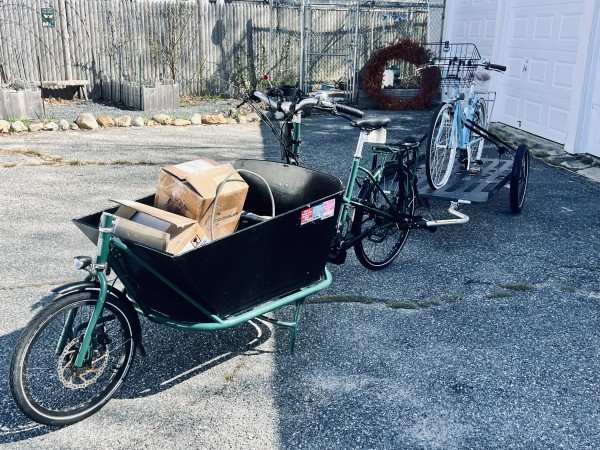 A Cetma Cargo bike with the front box filled with boxes and an attached Hinterher trailer with a bicycle on it.