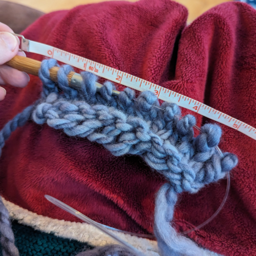 A partial swatch of my recently spun handspun. There are 10 stitches on the needles and the measuring tape above shows that it's about 5 inches wide.