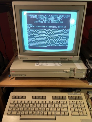 A Commodore 128D with a 1902A monitor on top showing the 10PRINT program and the output of random slashes. 