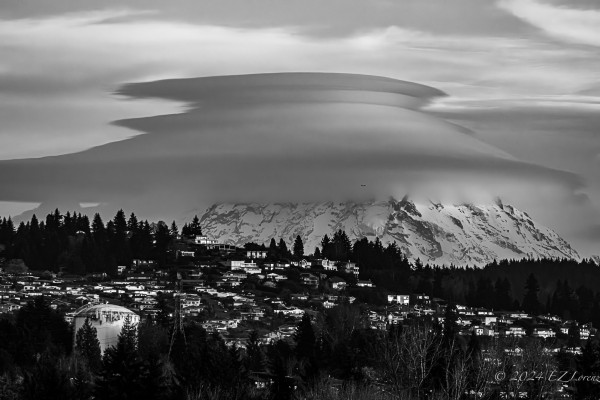 Black and white image of Tahoma with lenticular clouds. There’s a hilly residential area in the foreground. 