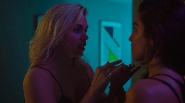 A screenshot from I Love Suzie (2020) of two people talking in a darkened bedroom at night. The colours are vibrant, her hair, the skin, yet somehow muted. 