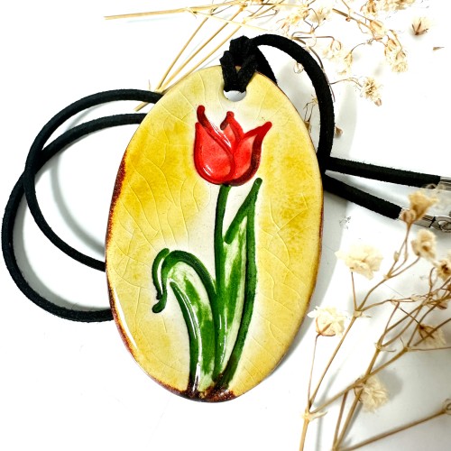 A handmade ceramic pendant with a tulip design by surlyramics. The tulip is red and green. The pendant itself is painted in a bronze crackle graze. 