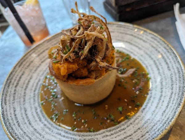 A tall pie topped with sweet potato puree and crispy onions on a plate surrounded by delicious gravy.