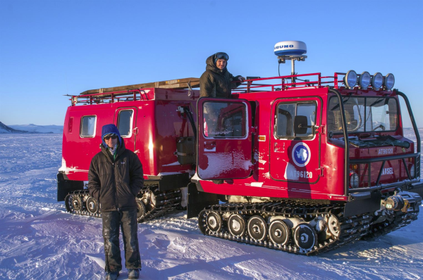 Antarctic explorers next to a tracked vehicle with red paint and official logo, lights... radar. Name on front is "Hansel"