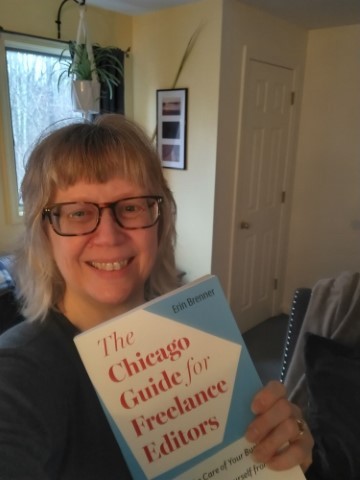 Editor Erin C. Brenner smiles because she is holding a copy of the book she wrote for the University of Chicago Press. It's The Chicago Guide for Freelance Editors: How to Take Care of Your Business, Your Clients, and Yourself from Start-Up to Sustainability.