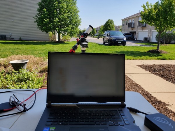 A laptop outside in the shade, with a telescope in the background. The laptop screen is redacted for your protection