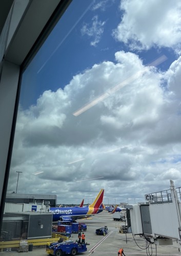 Blue sky with fluffy clouds. At airport, Southwest airplane in the picture. All taken through a window. 