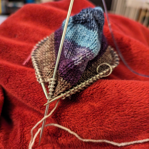 A sock toe knitted from self striping yarn. Most of the stitches are on a small circular needle but a few have been transferred to a larger needle as I prepare flip the small circular around to face the right direction.