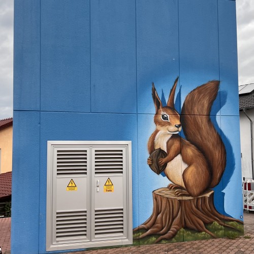Mural of a squirrel on a tree stump on a blue building wall, next to industrial gray doors marked "Trafo" with warning signs.