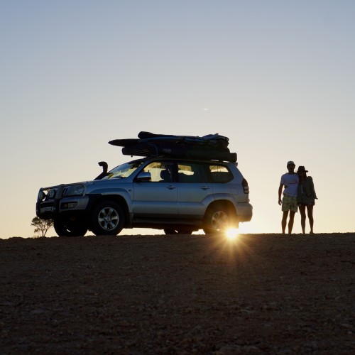 The sun in rising over Mundi Mundi lookout near Broken Hill in New South Wales. We can see the silhouettes of a couple and a car. 
