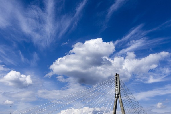 very blue sky with white clouds and top of a bridge tower piercing the sky