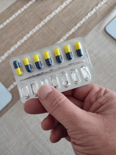 Eight pill capsules in blue and yellow in a blister pack. One is inverted in the pack
