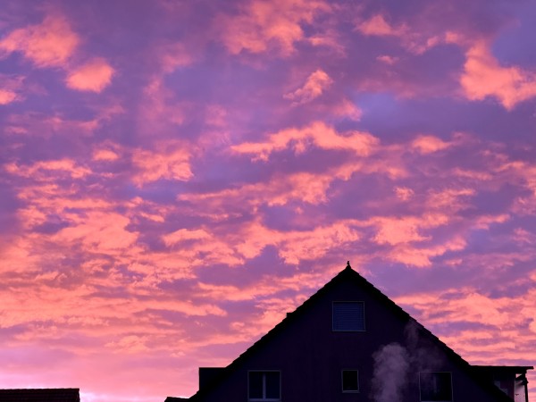 A vibrant sunset with pink and purple clouds above the silhouette of a house.
