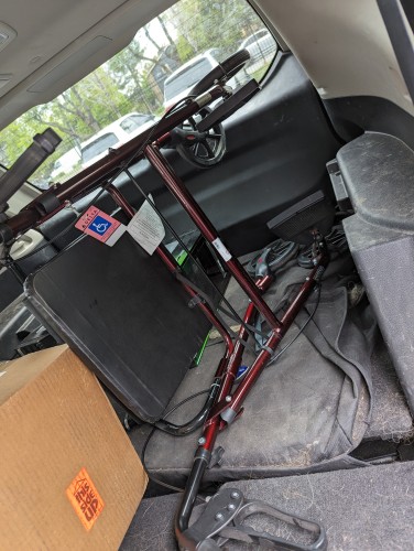 a rollator folded laying in a vehicle with folded down seats. the rollator is metallic maroon with black parts