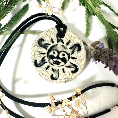 A ceramic pendant with a smiling sun design painted in a cream crackle glaze. 