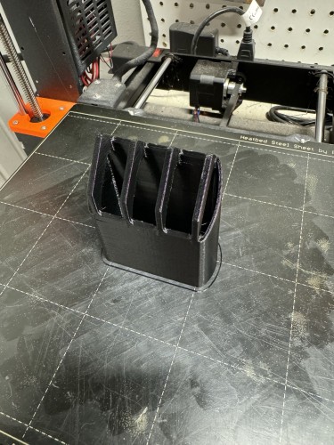 A black 3D-printed object on a 3D printer's bed.
