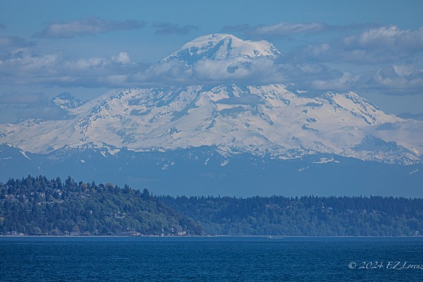 Telephoto view of Tahoma towering over the blue waters of Puget Sound, few clouds hanging toward the top of the mountain. Taken from a ferry. 