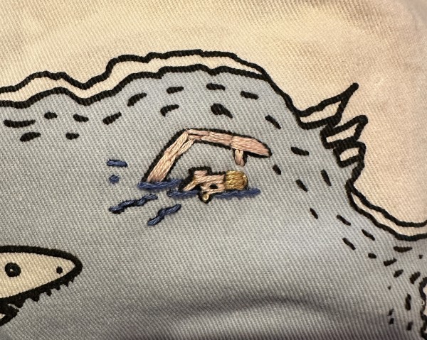 A small embroidered swimmer. Half the face is visible above the water as is one arm (doing front crawl). 