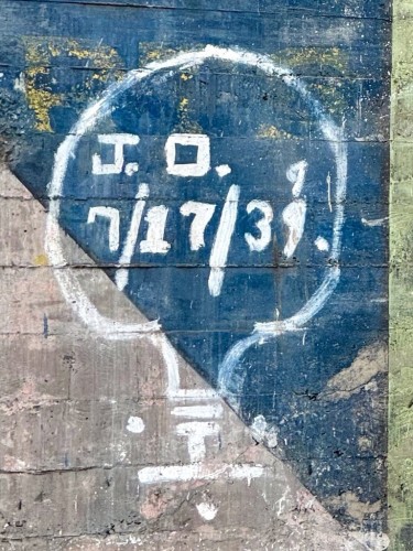 A close up of the ghost sign, where you can see someone drew a lightbulb in white paint and wrote "J.O. 7/17/39" inside the light bulb. It looks like they were unhappy with how their "9" turned out, so they crossed it out and wrote a better looking "9" above it.