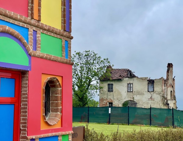 A colorful building corner juxtaposed against a dilapidated, partially collapsed structure in the background, under an overcast sky.