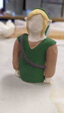 A picture of a small ceramic figurine of Link from the waist up, wearing his signature green outfit.