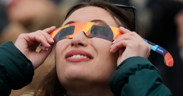 a stock photo of a woman looking up at the sky with eclipse glasses on