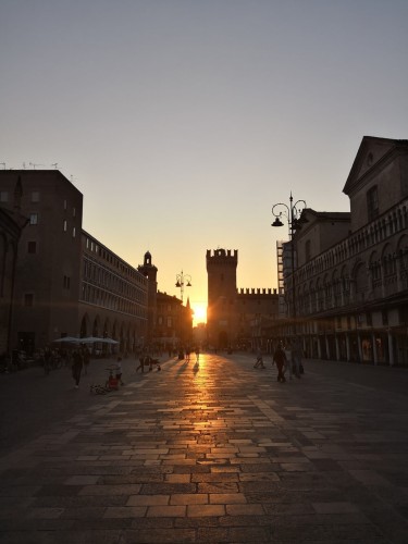 Sun is setting in Ferrara's main square.
Everything is orange, the sun is between the tower and an ancient palace. Some people around, it's a warm, calming and relaxing photo.