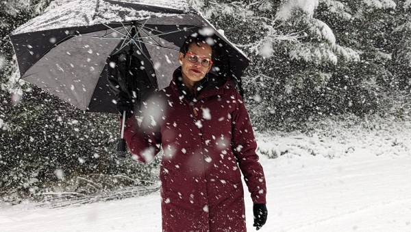 Kate looking vaguely irritated standing in a lot of snow while more snow falls on her clearly inadequate umbrella.