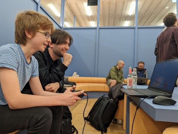 Emi watching the young developer showcase his Godot game on a laptop with controller