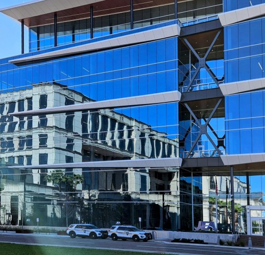 Large downtown building adjacent to the county court house.  Three stories of large clear windows reflect near perfect reverse images of the clear blue sky and the large court house.