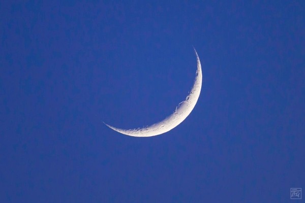 a thin crescent of moon on a blue sky