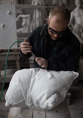 A photo showing artist Hakon Anton Fageras working on a marble sculpture that is shaped like a soft pillow.
