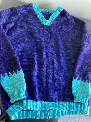 A handknit purple V-neck sweater with turquoise trim at neck, hem, and bottom quarter of sleeves.