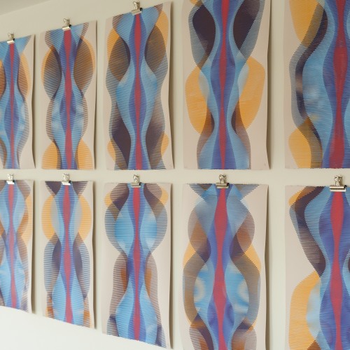 10 abstract paintings arranged in a grid, hung on a white wall with metal clips. Each painting has a variation of red, blue, and yellow ochre acrylic paint on pearl gray paper.