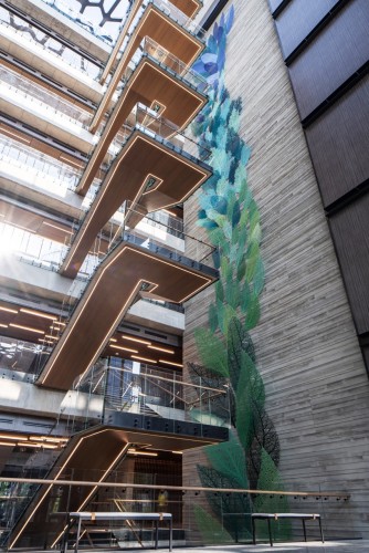 Bent metal leaves climb up a 9 story tall atrium next to a cantilevering staircase. They shift from green to blue as they approach the skylight