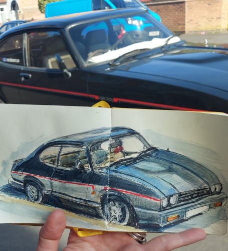 The lower half of the photograph shows a sketchbook and in it, drawn over two pages is a black, boxy car with a red stripe along the side. Above it we can see the real life car, parked on the side of the road.